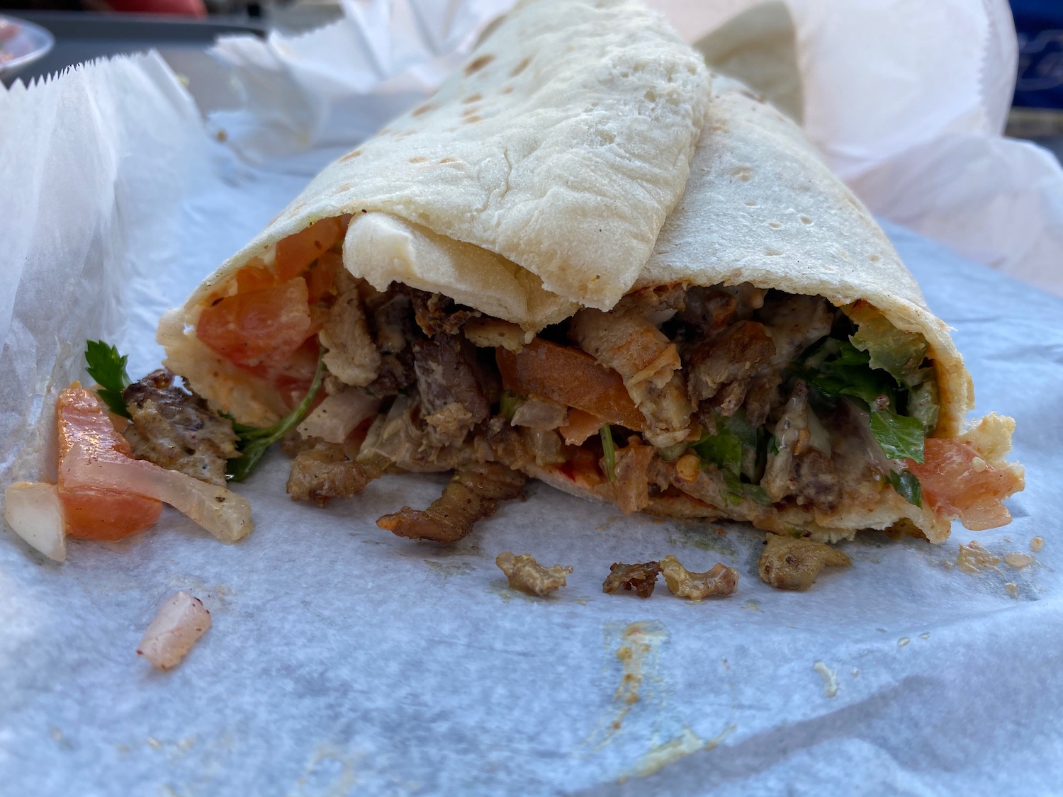 a burrito with meat and vegetables on a white paper