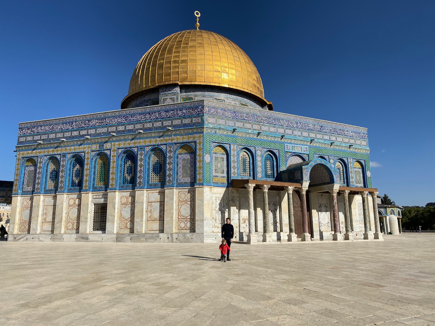 a man and a child standing in front of Dome of the Rock